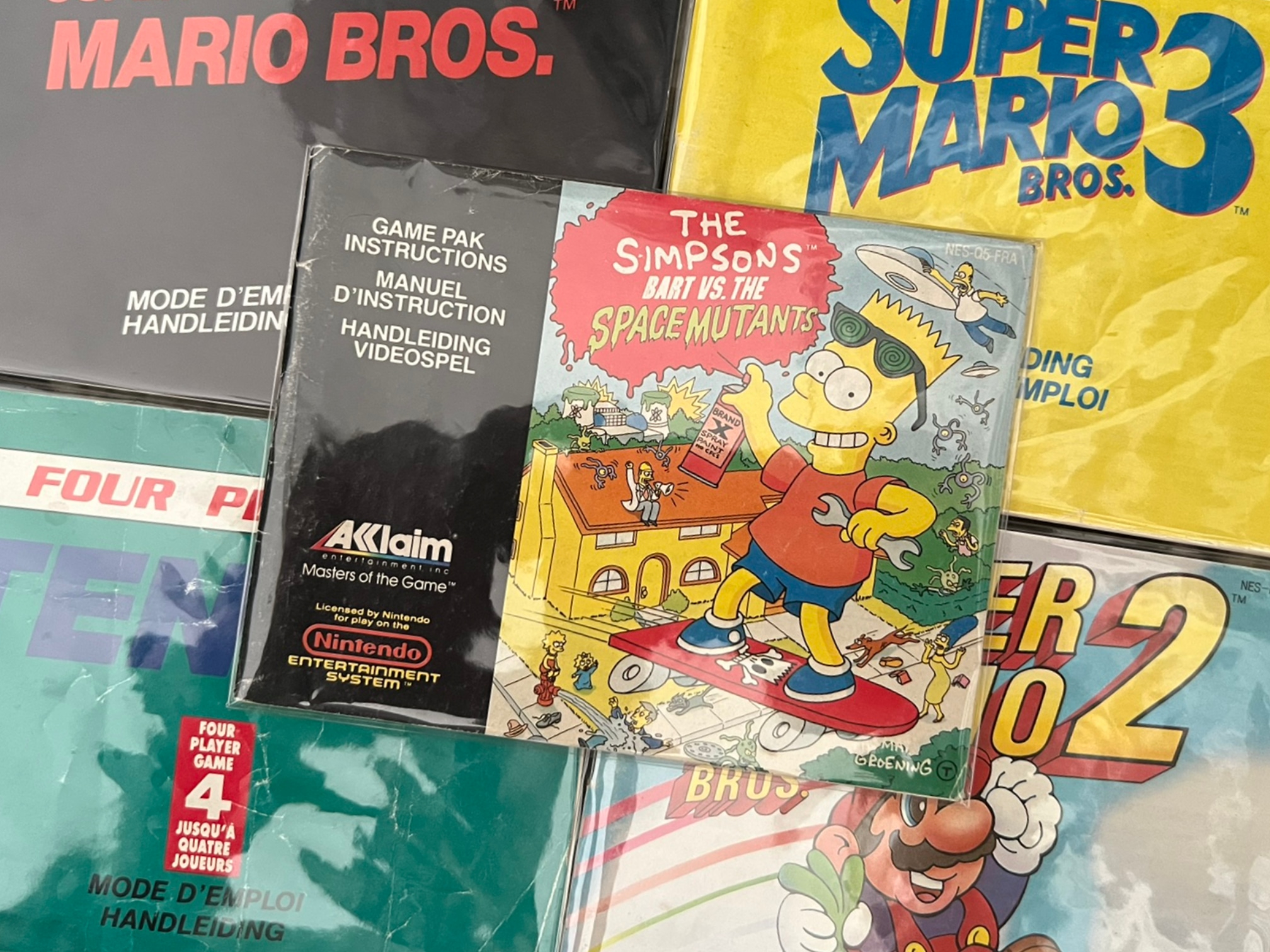 Close up of NES manuals from Super Mario Bros 1, 2 and 3, Tennis, and Bart vs Space Mutants